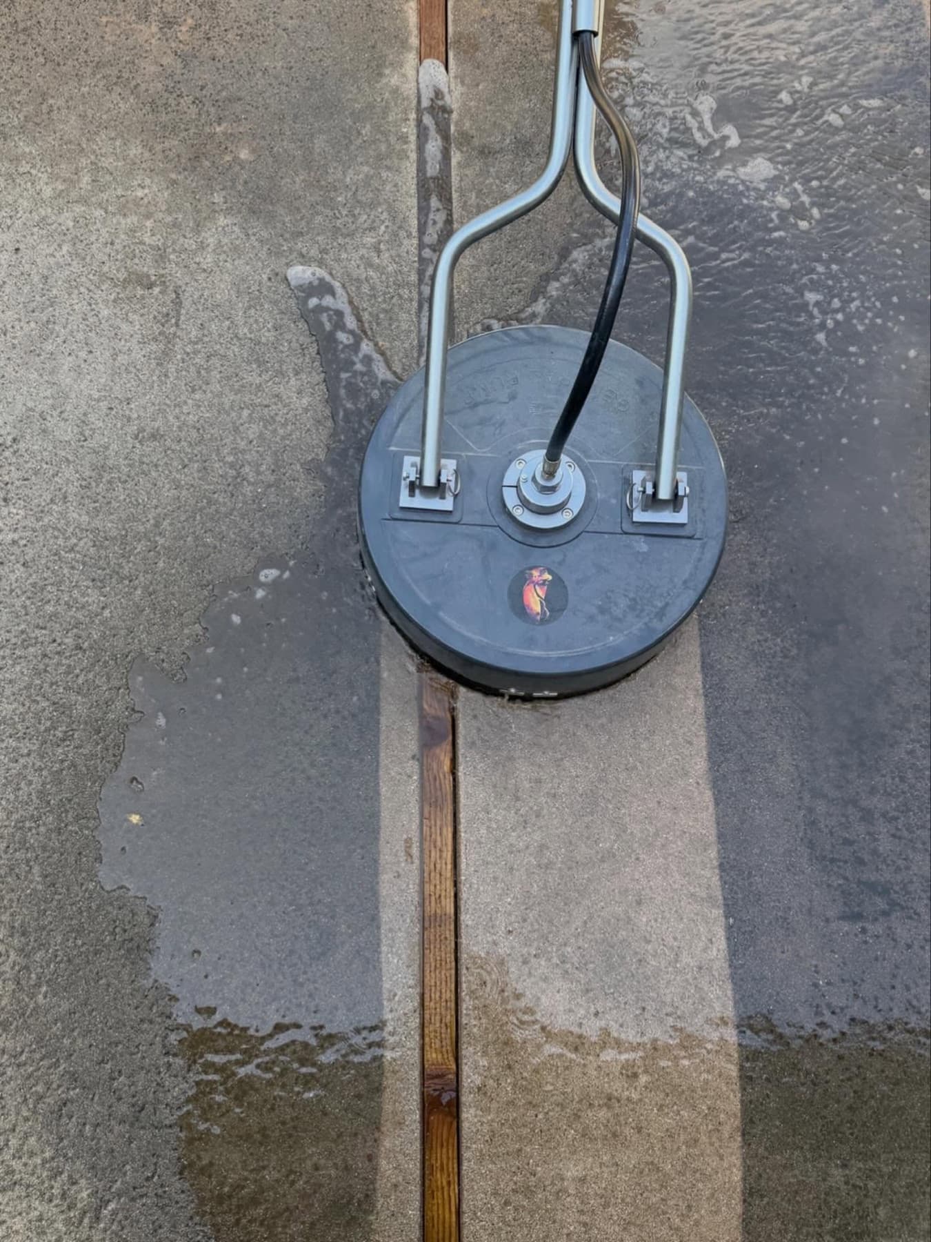 Surface cleaner cutting a clean line through a dirty driveway in Huntington Beach