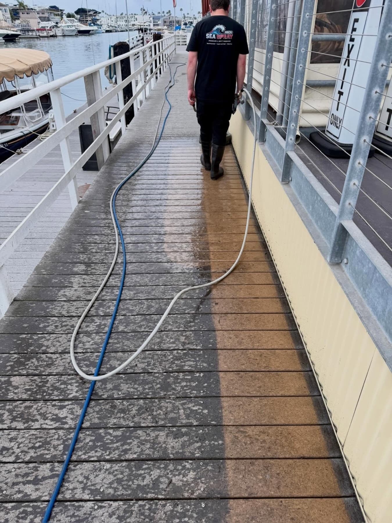 Sea Spray Pros technician pressure washing a marina dock boardwalk in Huntington Harbour with boats behind